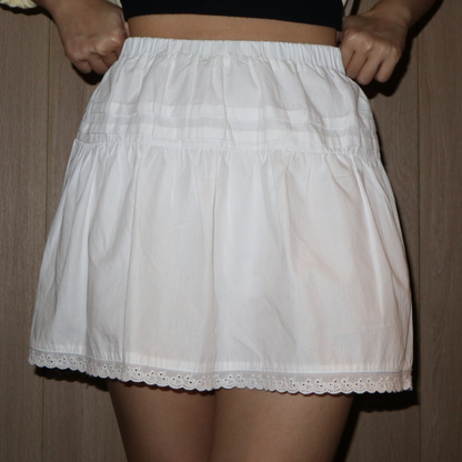 A white mini skirt with a flared design and lace detailing at the hem.