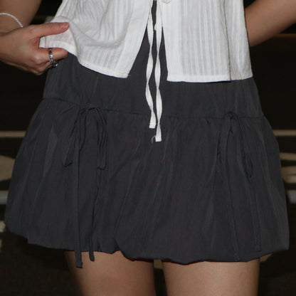 A black bubble skirt with double ribbons tied at the waist, worn with a white striped top.