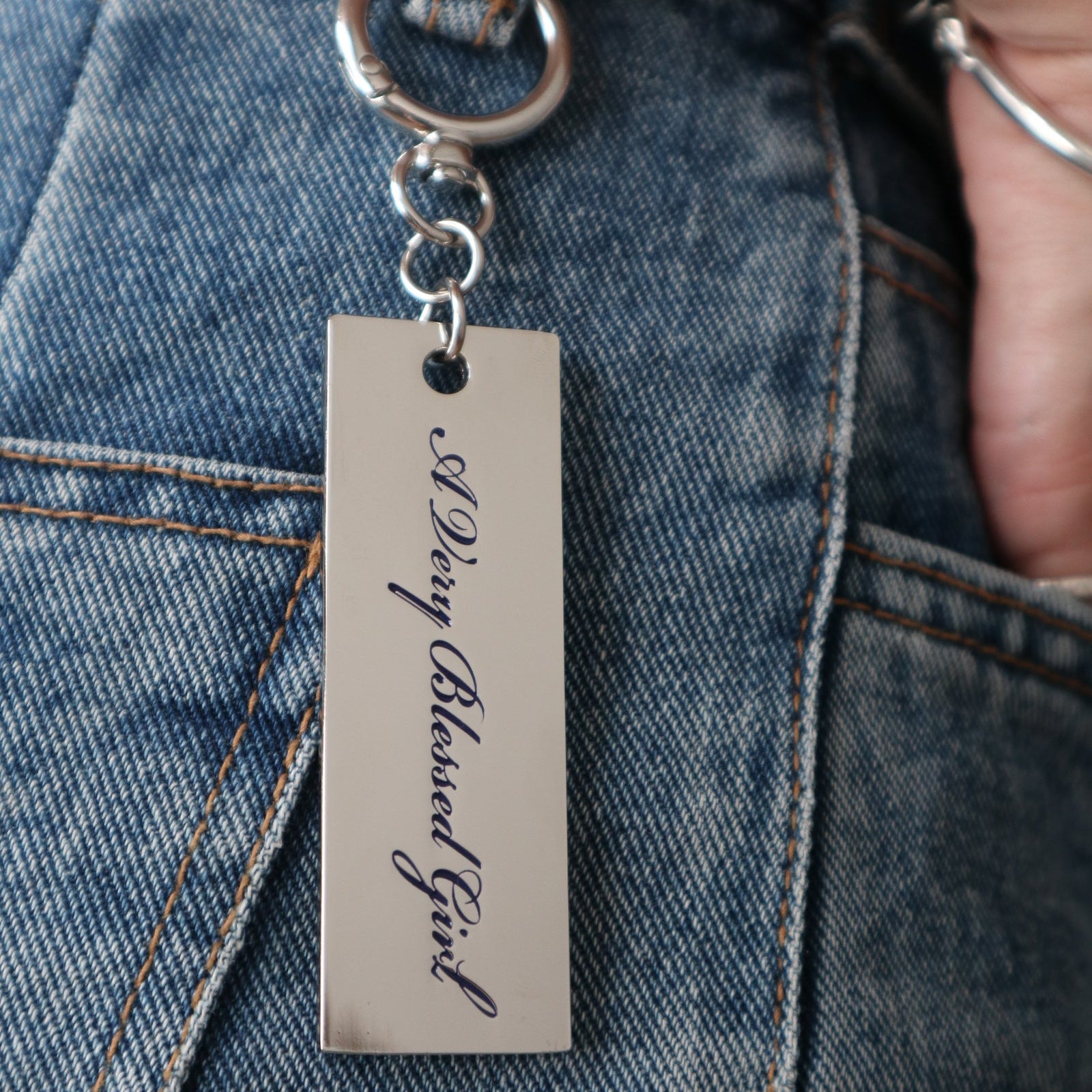 Metal kaychain with engraved text hanging on a denim jeans belt loop