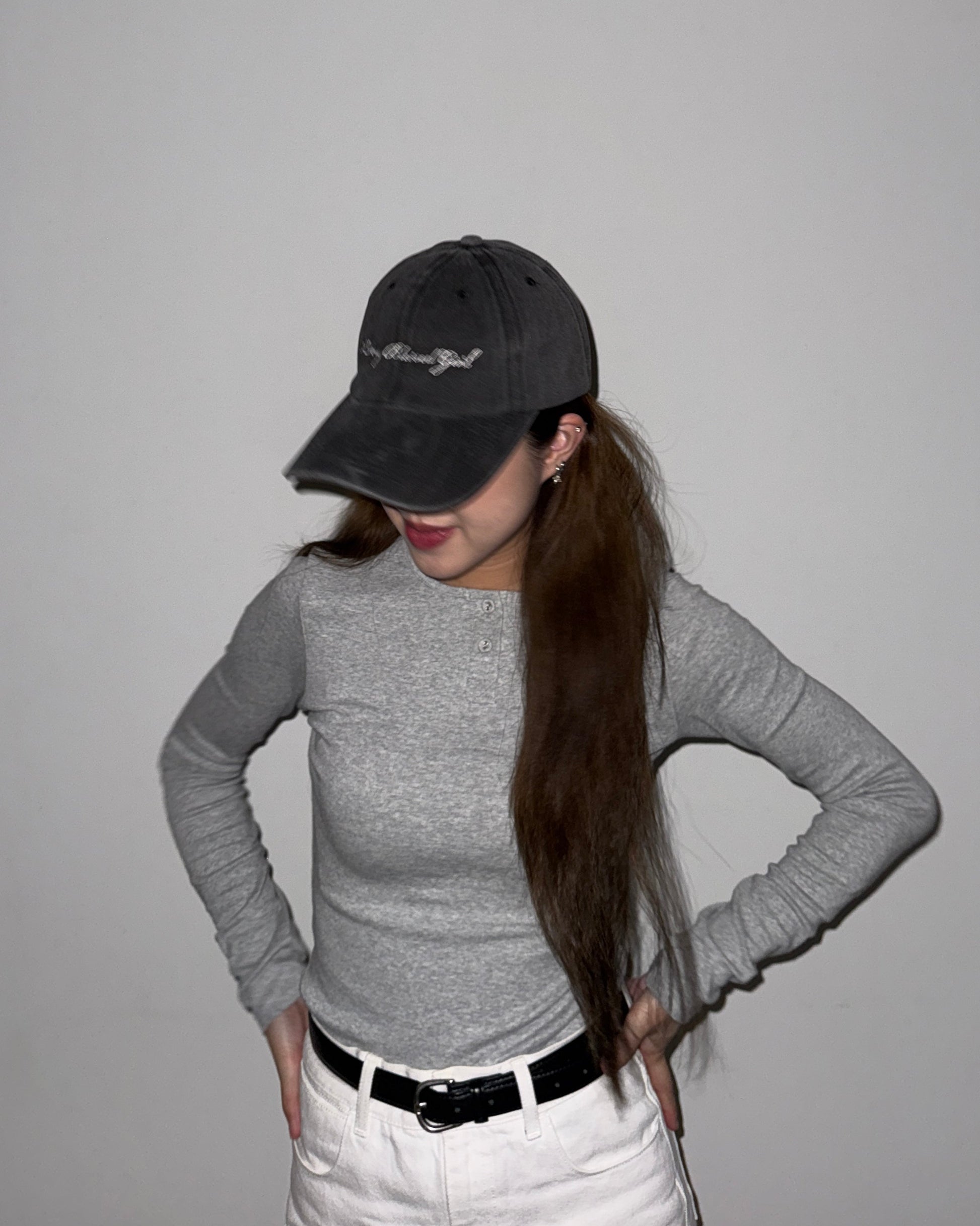 Person wearing a gray long-sleeve shirt, black cap, and white pants against a plain background