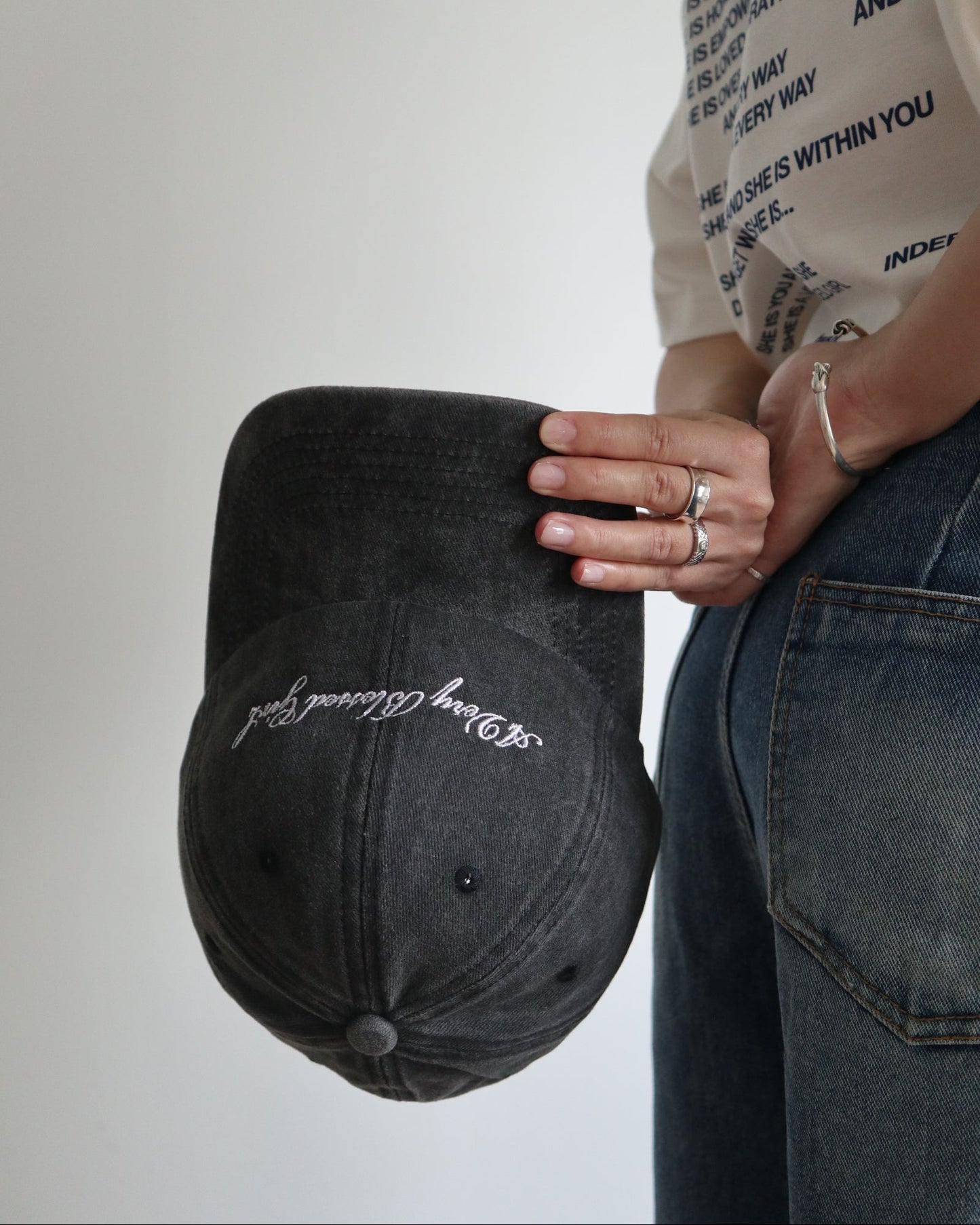 Person holding a black washed cap with embroidered text