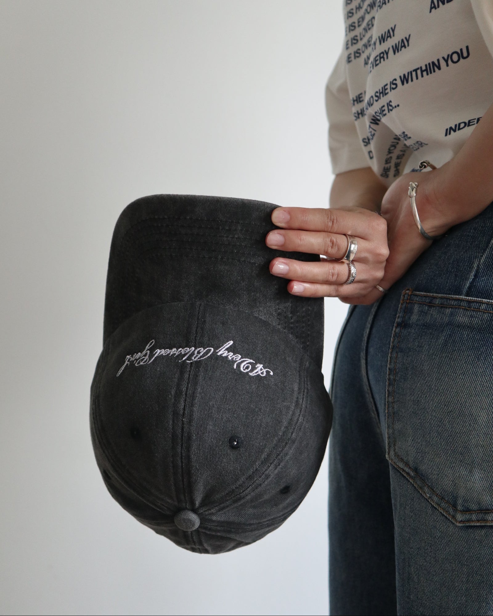 Person holding a black washed cap with embroidered text