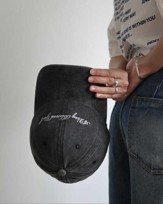Person holding a black washed cap with embroidered text