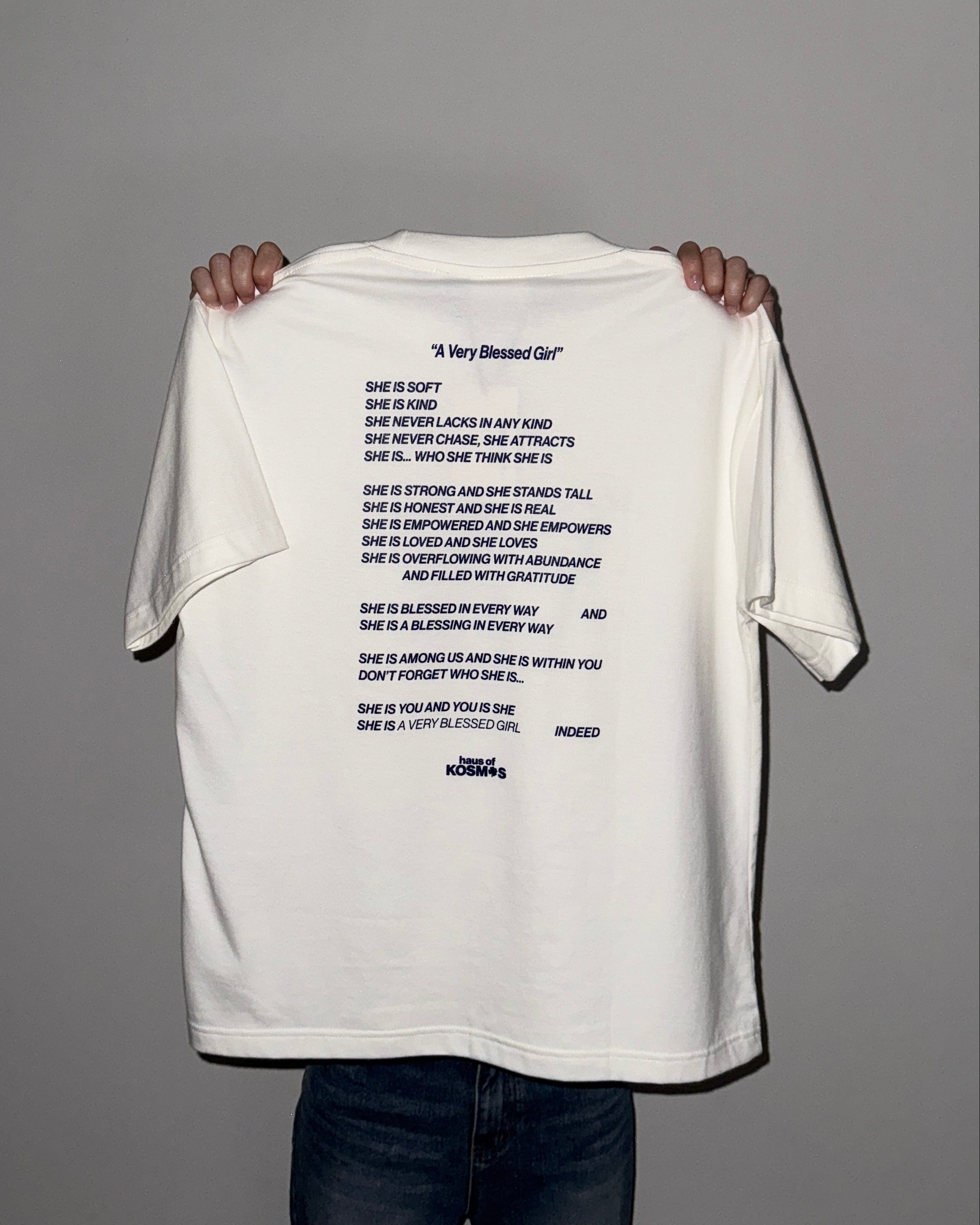 White t-shirt with text held by a person against a gray background